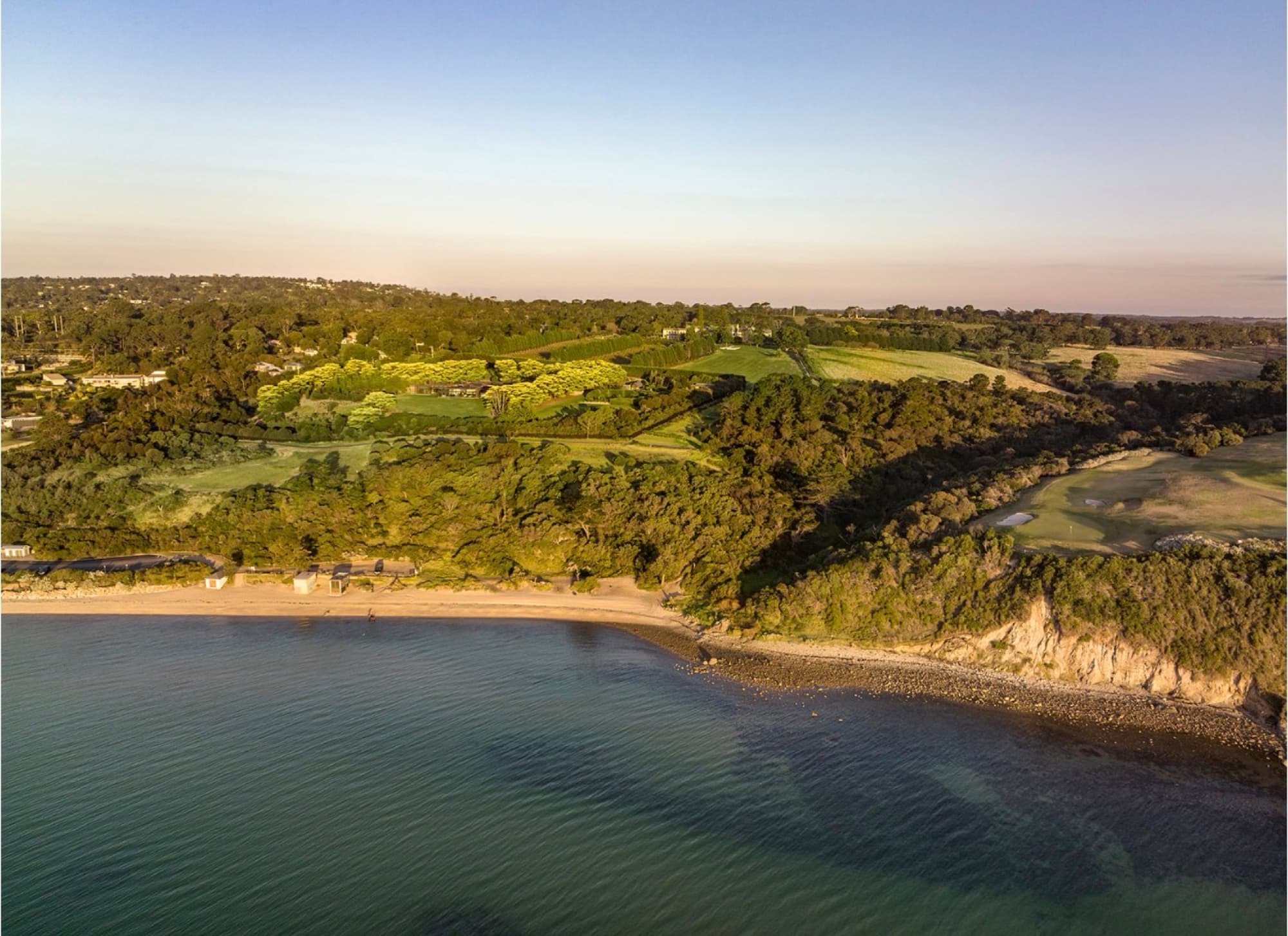 Sunnyside Estate from over the water at golden hour — the beach, the cliff and the gardens above